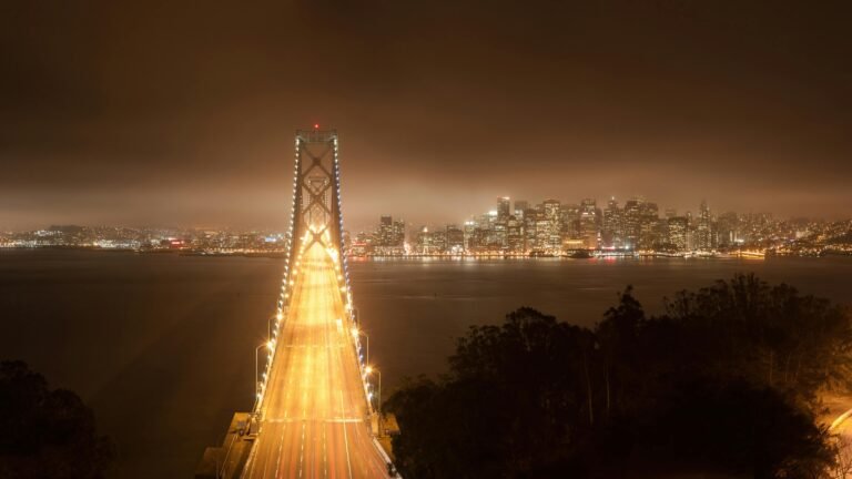 10 Awesome Things to Do in San Francisco + Best Hotels to Stay Aerial view of the Golden Gate Bridge leading to illuminated San Francisco skyline at night.